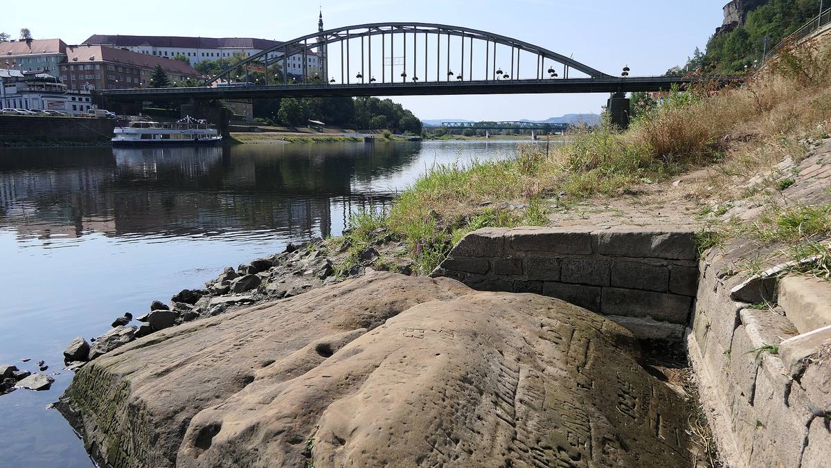 Hladový kámen s vytesanými letopočty na břehu Labe v Děčíně, v pozadí obloukový most
