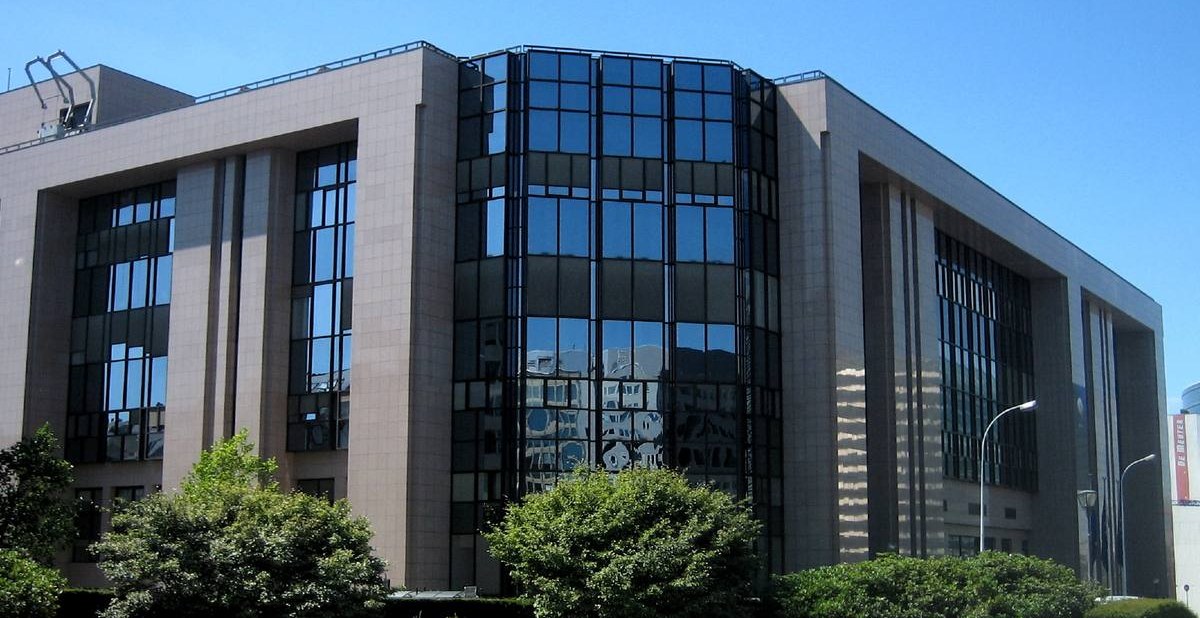 Prosklené nároží kamenné budovy Justus Lipsius v Bruselu za vzrostlými keři