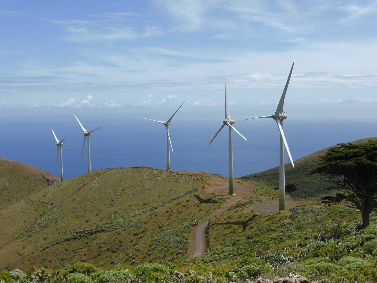 Pět velkých větrných turbín na travnatém hřebeni ostrova El Hierro, za nimi Atlantský oceán
