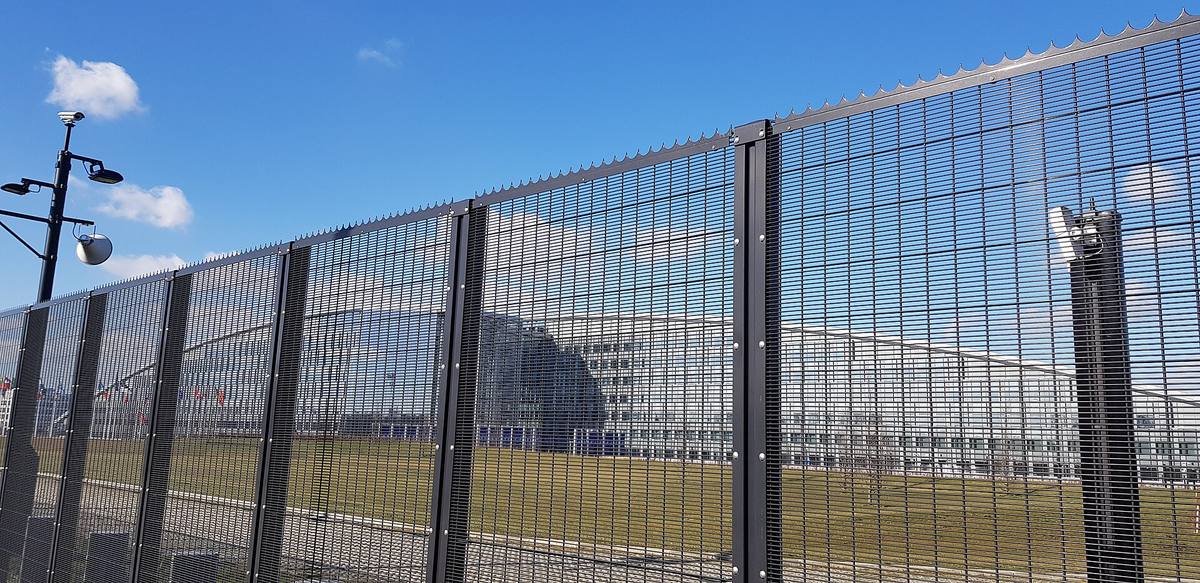 Vysoký plot z ocelových mříží, za ním trávník a budova sídla NATO v Bruselu