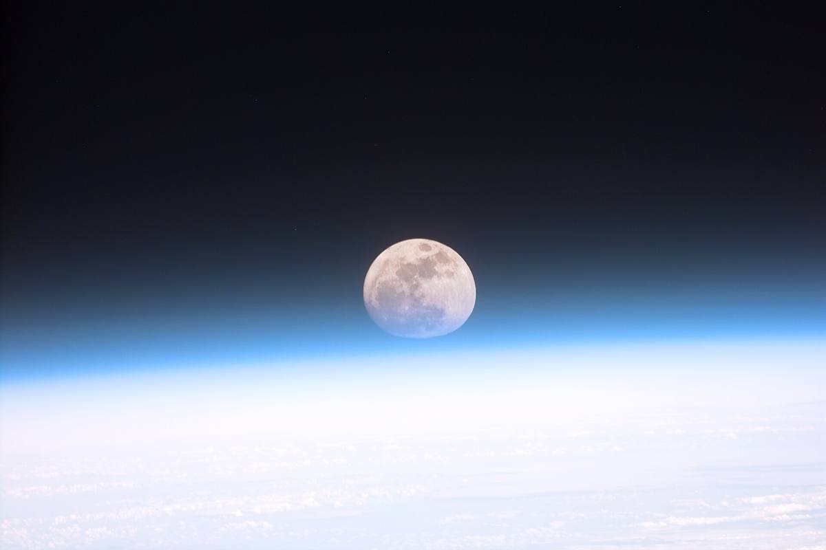 Měsíc v úplňku nad modrým pruhem zemské atmosféry, snímek z vesmírné stanice