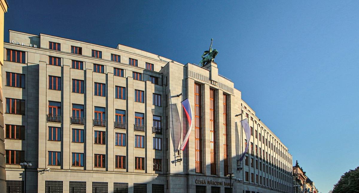 Funkcionalistická budova České národní banky na Příkopech s vlajkami a jezdeckou sochou na střeše.