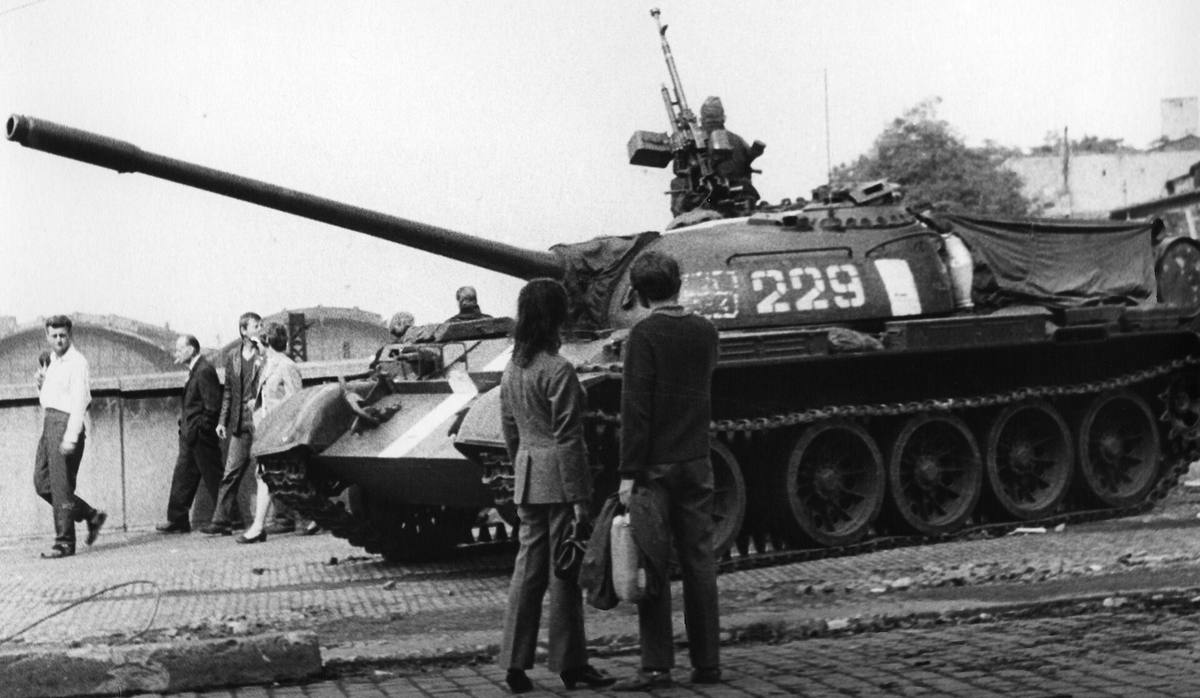 Sovětský tank T-55 s bílými identifikačními pruhy stojí v srpnu 1968 na pražské ulici, kolem něj chodci